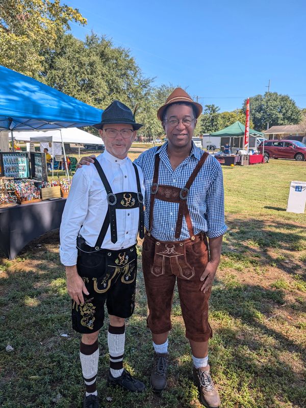 Two men wearing traditional lederhosen at an outdoor fair.