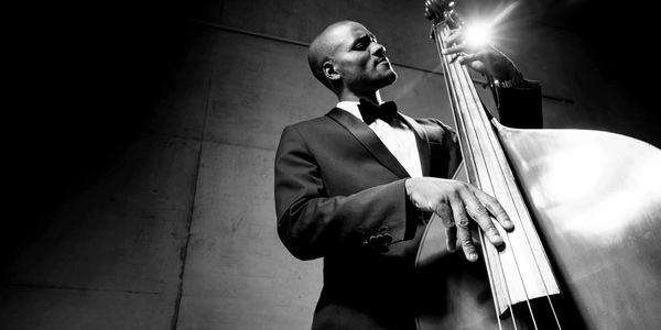 A musician in a tuxedo passionately plays a double bass under dramatic lighting.