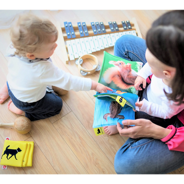 An adult and a child reading a colorful animal book on the floor with musical instruments nearby.