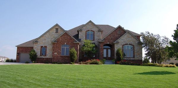 Spacious brick and stone house with a large green lawn under a clear sky.