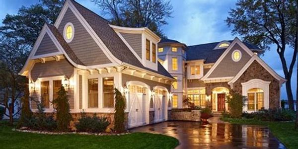 Elegant, large house with warm lighting and wet driveway at dusk.