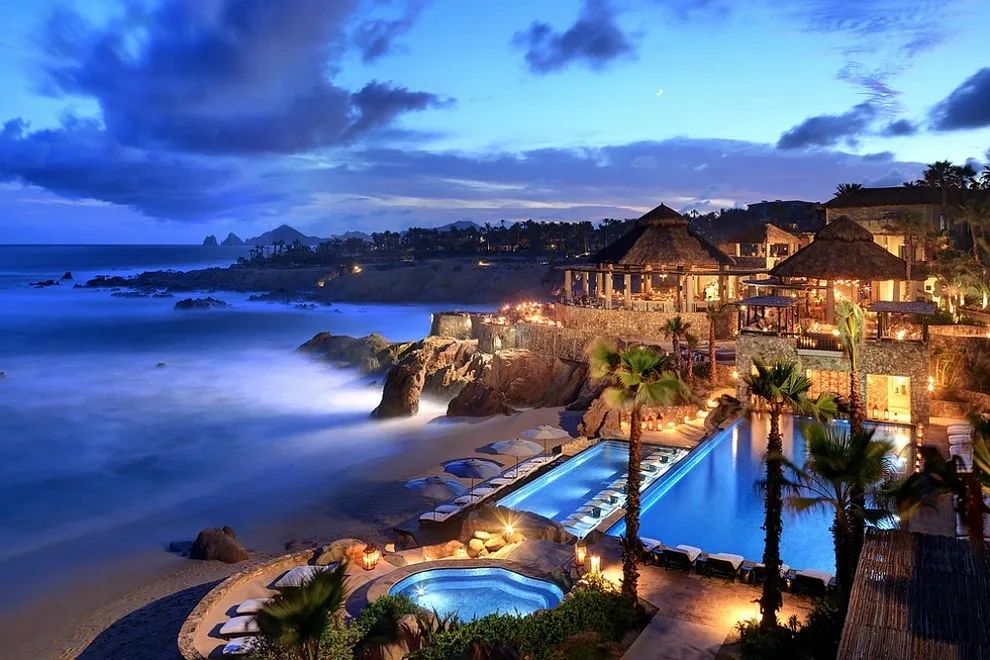 Luxurious beachfront resort at twilight with illuminated pools and ocean views.