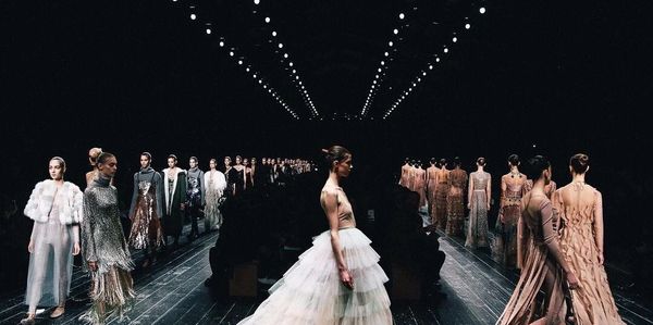 Models showcasing elegant dresses on a runway under bright lights.