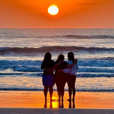 Three people embracing while watching a vibrant sunset over the ocean.