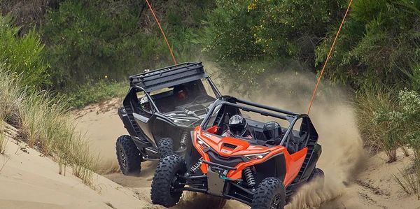 Two off-road vehicles racing through sandy terrain kicking up dust.