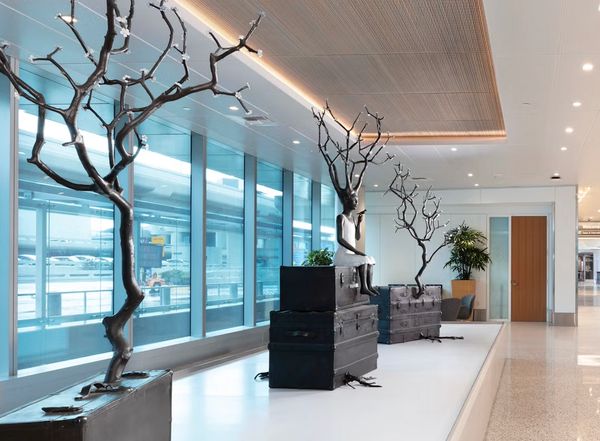 Artistic sculptures of tree-like figures and a seated figure on suitcases in a modern indoor space.
