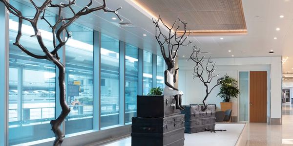 Artistic sculptures of tree-like figures and a seated figure on suitcases in a modern indoor space.