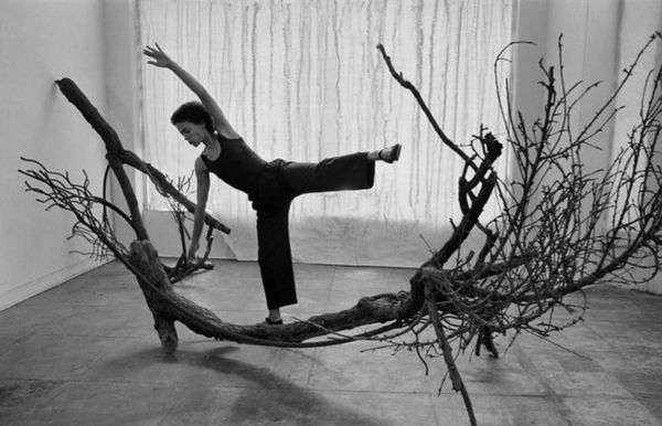 A woman balancing on a large tree branch installation indoors.