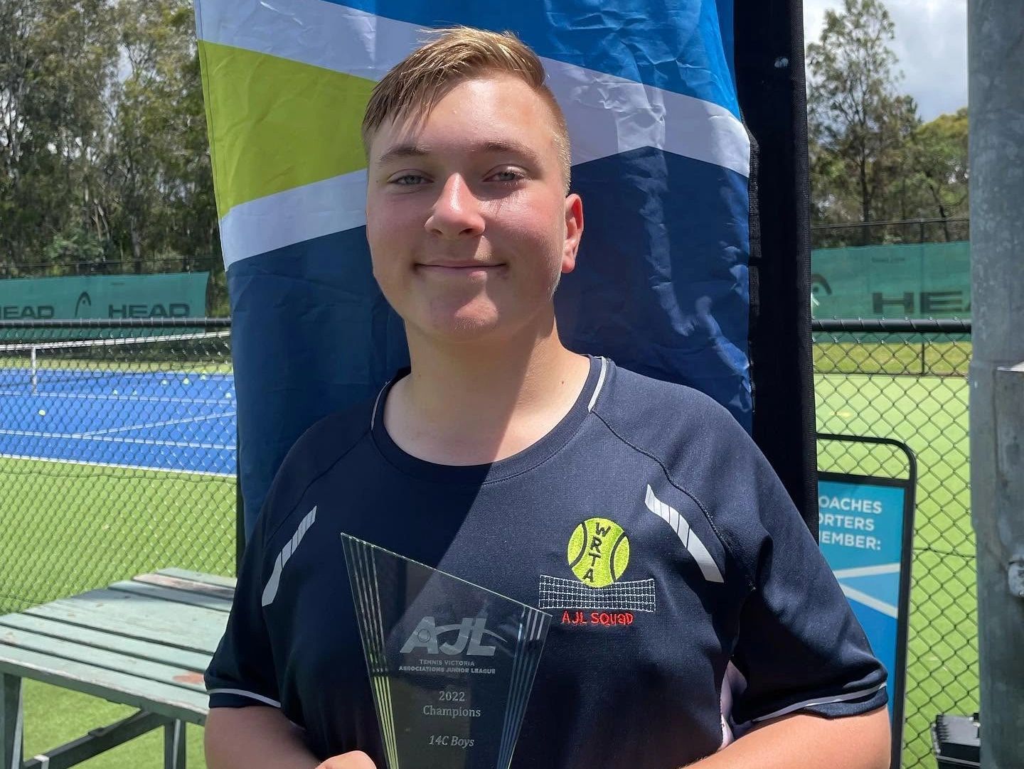 Young tennis player holding a 2022 champion trophy.