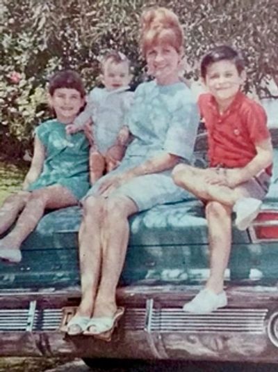 Familia de los años sesenta sentada sobre un automóvil sedan azul.