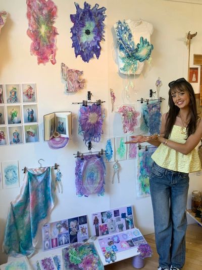 Young woman proudly presenting her colorful abstract art display on a wall.