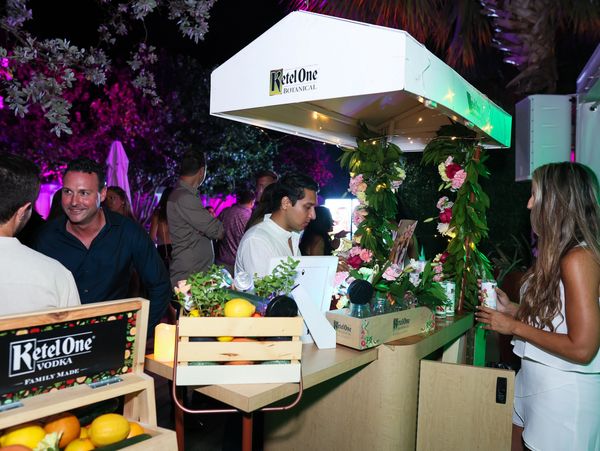 People enjoying a nighttime Kettle One Botanical vodka booth decorated with flowers and greenery.