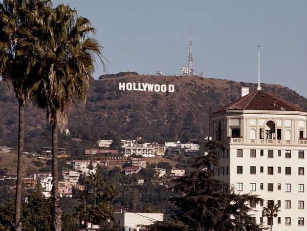 Hollywood sign on a hill with buildings and palm trees in the foreground.