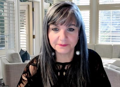 Woman with long gray hair and pearl earrings in a bright living room.