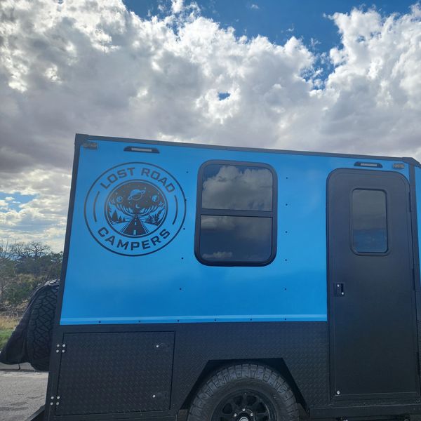 Blue Lost Road Campers trailer under a cloudy sky.