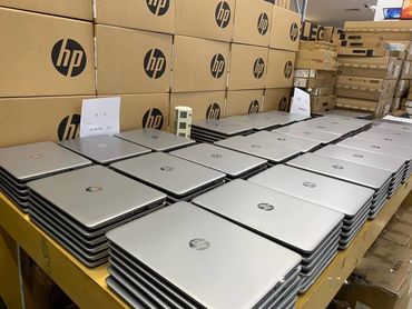 Stacks of silver HP laptops neatly arranged on a table in a storage area.