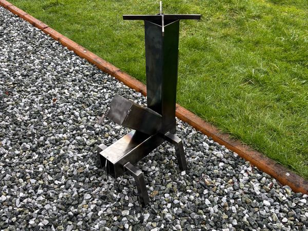 Black metal firewood splitter on a gravel surface with grass in the background.