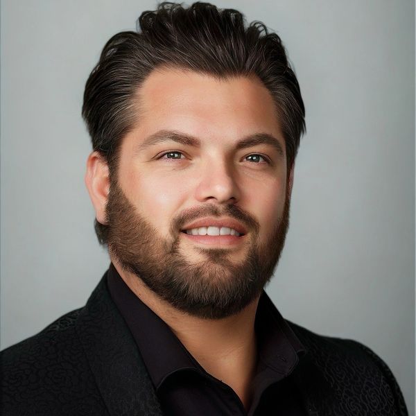 Smiling man with beard and dark hair in a black shirt and jacket.