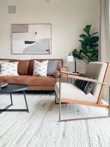 Model apartment living room with camel sofa, modern chairs, and abstract art at Axis 3700 in Texas