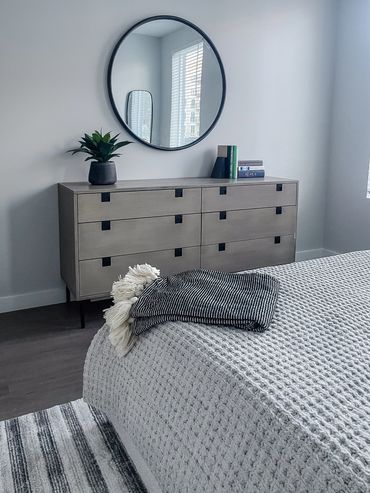 Multifamily model unit bedroom design with light wood dresser and round mirror at High Street