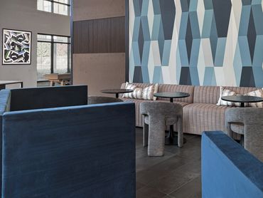 Close-up of blue geometric wallcovering with channel-tufted banquette and gray barrel chairs at Wind