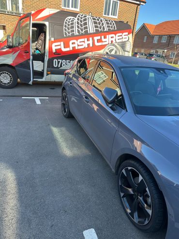 A grey car parked beside a Flash Tyres van with its door open.