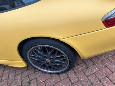 Yellow sports car with a flat rear tire parked on a brick driveway.