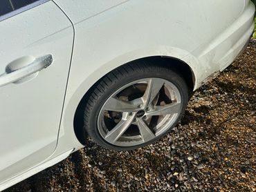 Close-up of a white Audi car's rear wheel and tire on a gravel surface.