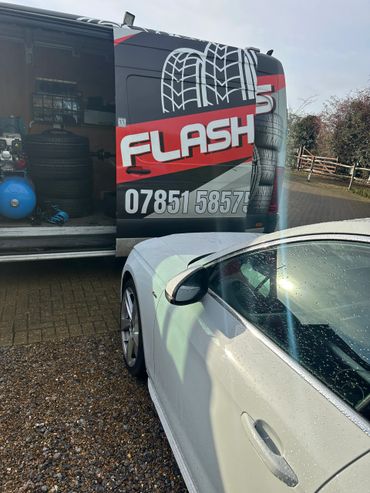 Van with tire service branding next to a wet white car in a driveway.
