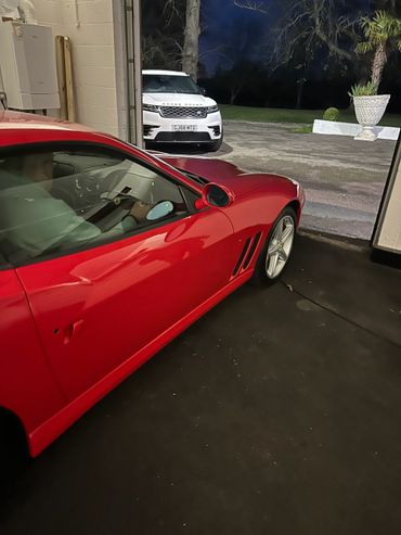 A red sports car parked inside a garage with a white Range Rover outside at night.