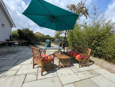 Outdoor patio with space for relaxing and dining and a large green umbrella and BBQ.