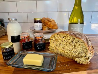 Welcome hamper with bread, butter, milk, croissants, jam, sauces, and a bottle of wine.