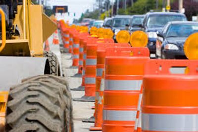 Orange traffic barrels lined up along a busy road under construction.