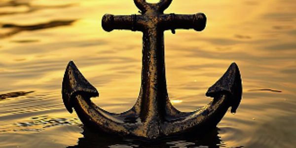 A black anchor partially submerged in golden water at sunset.