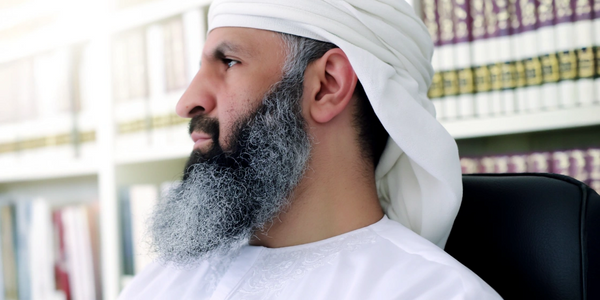 Profile of a thoughtful man with a white turban and beard in a library.