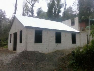 Unfinished house with concrete walls and a metal roof in a wooded area.