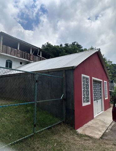Small red building with white doors and windows beside a fenced grassy area.