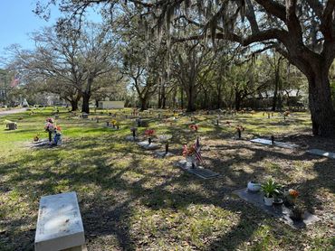 American flags and flowers beside memorial markers beneath live oaks at Beaches Memorial Park