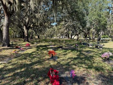 Flowers and memorial markers beneath oak trees at Beaches Memorial Park