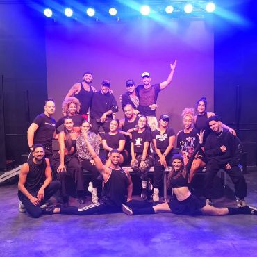 Large group of performers posing on stage under bright lights.