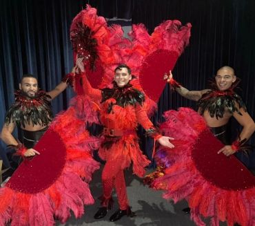 Three performers in vibrant red feather costumes posing with large fans.