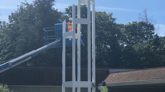 Workers painting a tall white church cross structure outside a building.