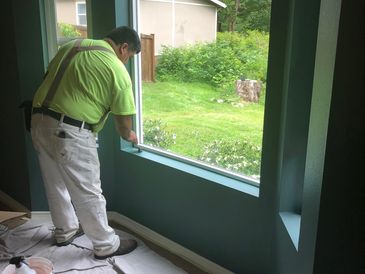 Painter working on window trim in a room with teal walls.