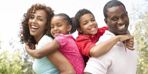 Happy family of four enjoying a piggyback ride outdoors.