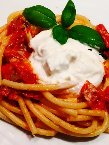 Plato de espaguetis con salsa de tomate fresco y una porción de burrata cremosa encima.