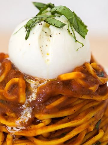 Plato de tonnarelli en salsa de tomate con una bola de burrata entera encima.
