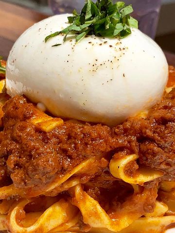 Plato de fettuccine a la boloñesa con una bola de mozzarella fresca encima.