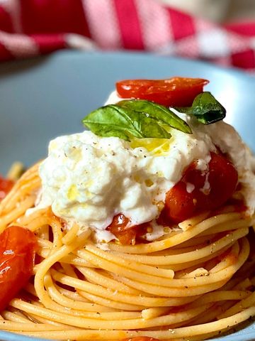 Plato de espaguetis con salsa de tomates cherry y porción de burrata cremosa encima.