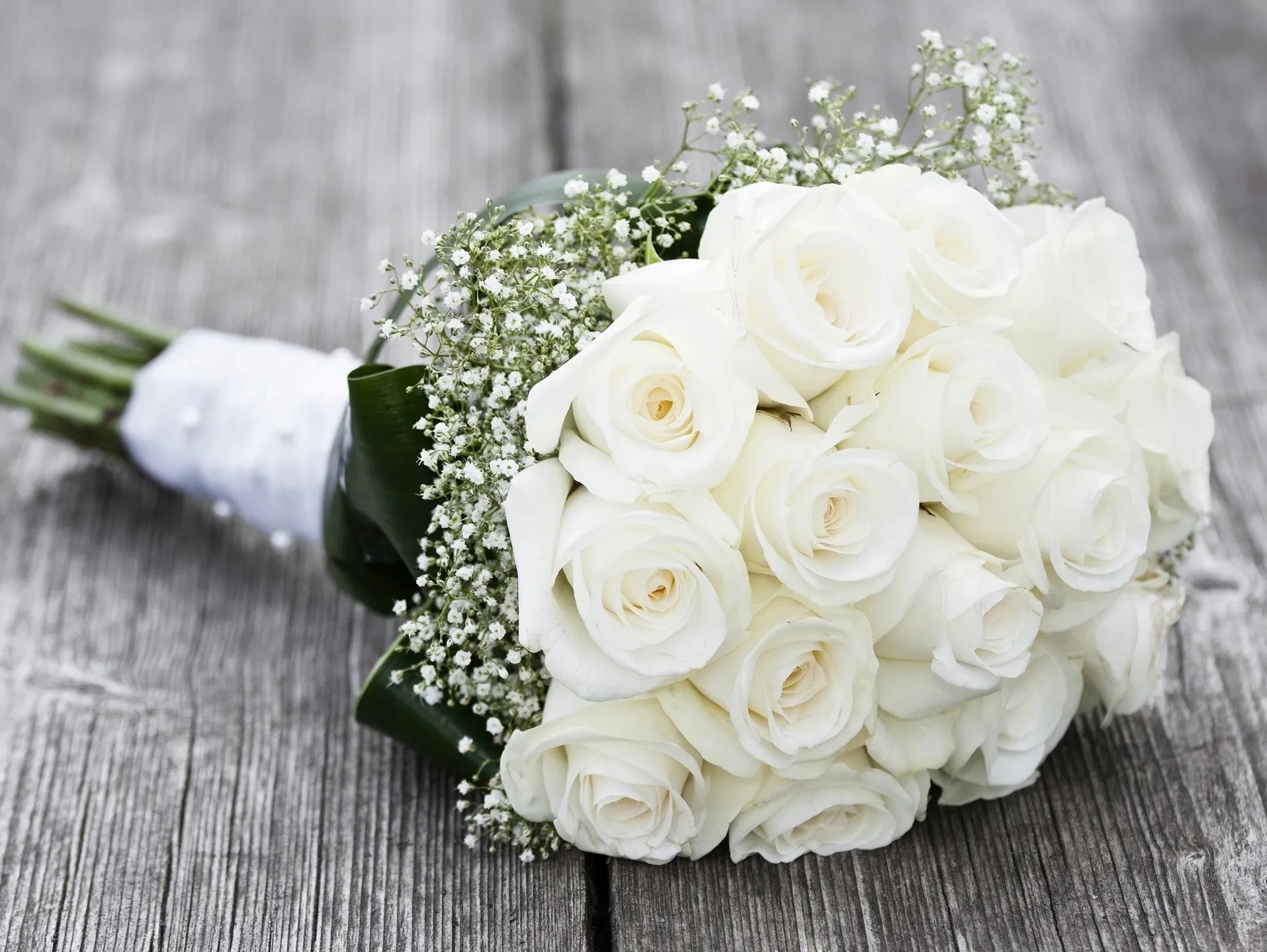 A bouquet of white roses with baby's breath on wood.