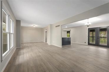 Spacious empty living area with light wood flooring and large windows.